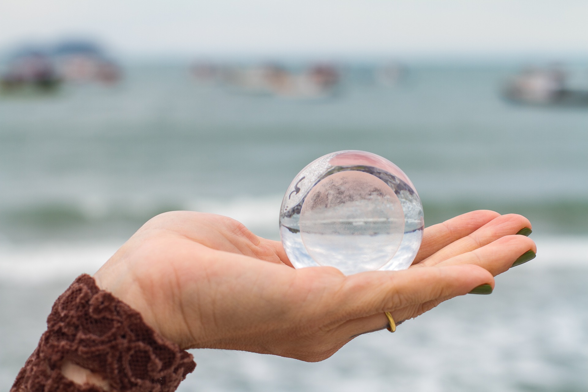 Esfera de cristal nas mãos com o mar ao fundo